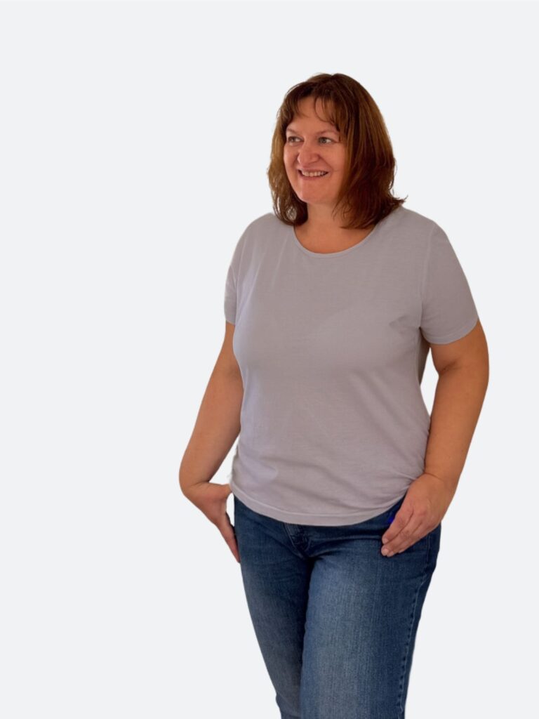 Mandy Egerland steht lächelnd vor einer hellen Wand und trägt ein hellgraues Shirt mit Jeans. Das Porträt wirkt ruhig, natürlich und authentisch.