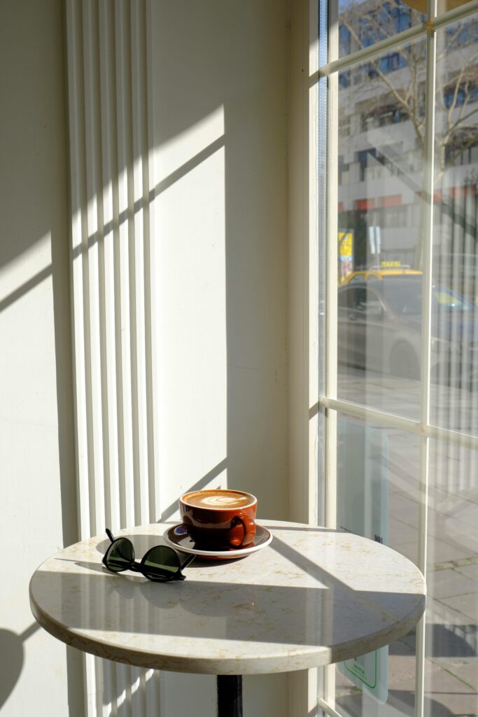 Personal Branding Impuls - Klarheit für den ersten Schritt Eine braune Tasse steht auf einem hellen Marmortisch im Sonnenlicht. Durch das Fenster fallen klare Schattenlinien, die Ruhe und Klarheit ausstrahlen - Symbol für bewussten Beginn und innere Ausrichtung.